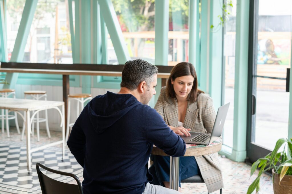 Two people glance at a computer in a cafe