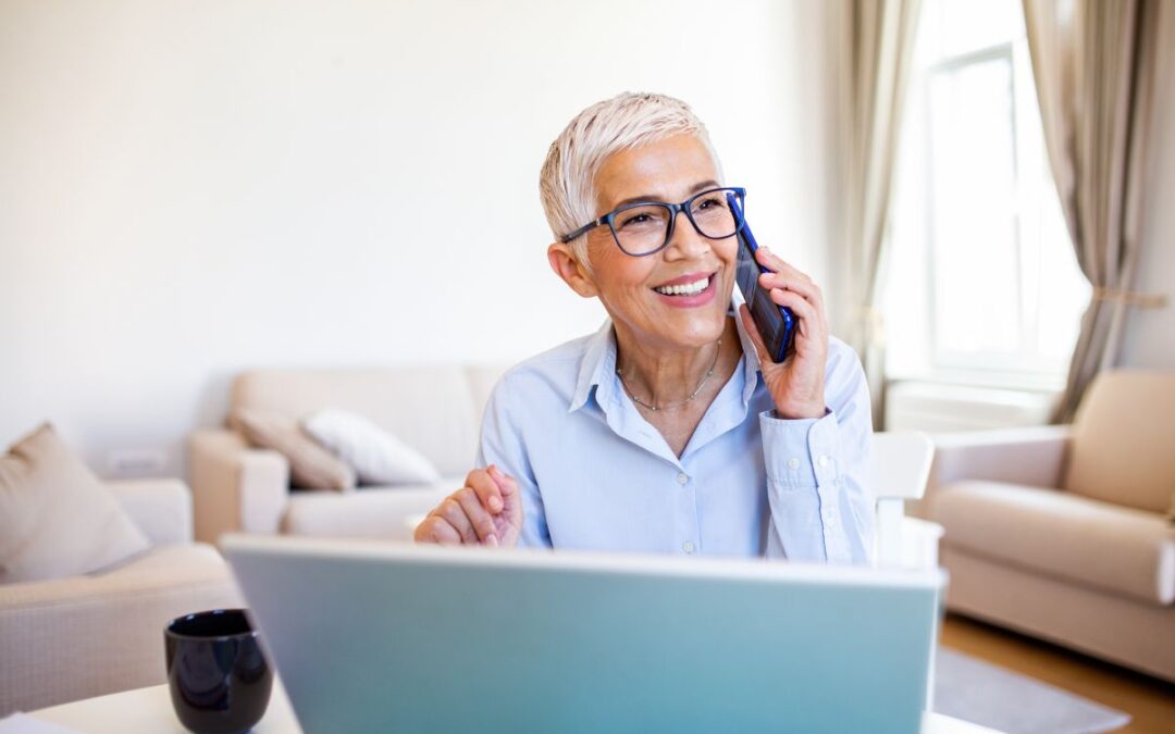 smiling woman on a cell phone sitting in front of a laptop computer in a living room setting