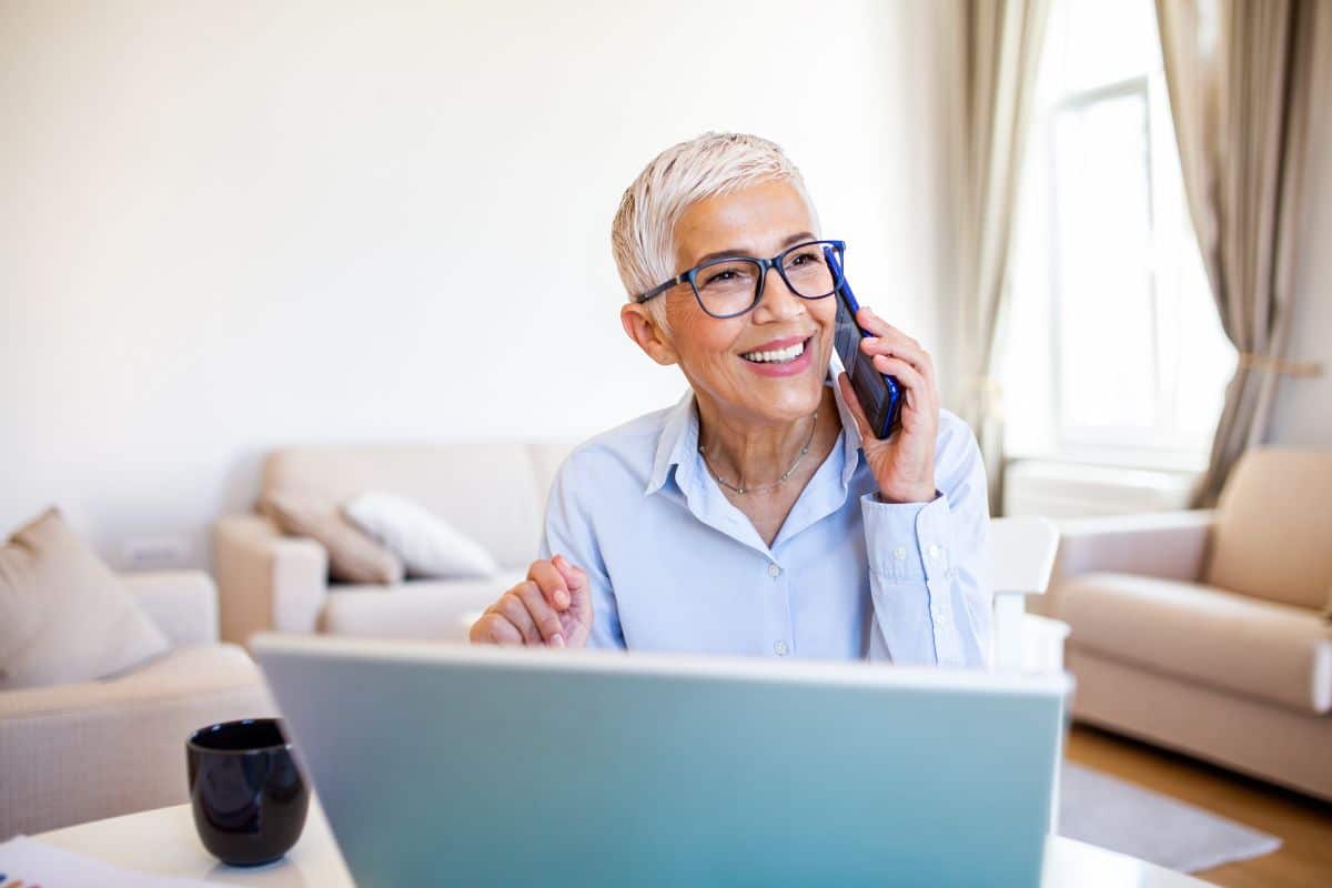 smiling woman on a cell phone sitting in front of a laptop computer in a living room setting