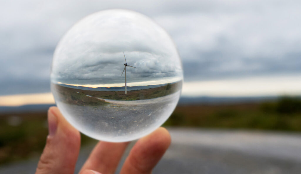 Wind turbine in glass ball in focus. Nature landscape out of focus in the background. Future of wind turbine and green energy production forecast and prediction concept.