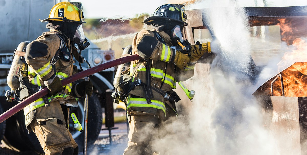 two firefighters turning a fire hose on an active flame
