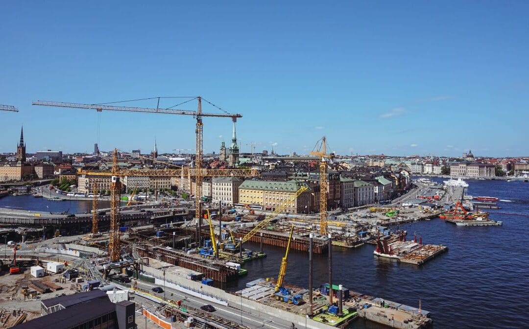 Aerial view of multiple infrastructure construction projects with cranes and waterfront development in a large urban area.