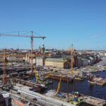 Aerial view of multiple infrastructure construction projects with cranes and waterfront development in a large urban area.