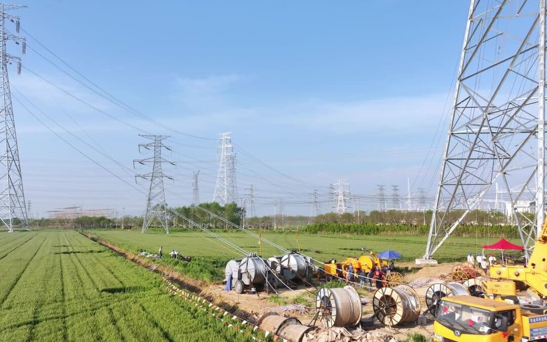 Construction scene with power line towers and workers under high voltage transmission lines in a green field