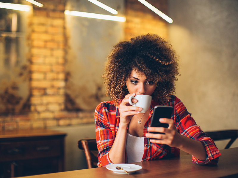 Woman using smartphone while drinking coffee in a cafe